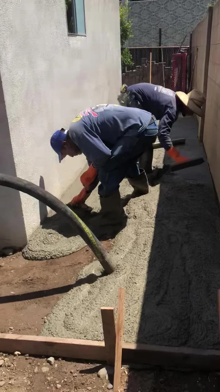 Crew placing concrete by pump hose into formed walkway along a block wall
